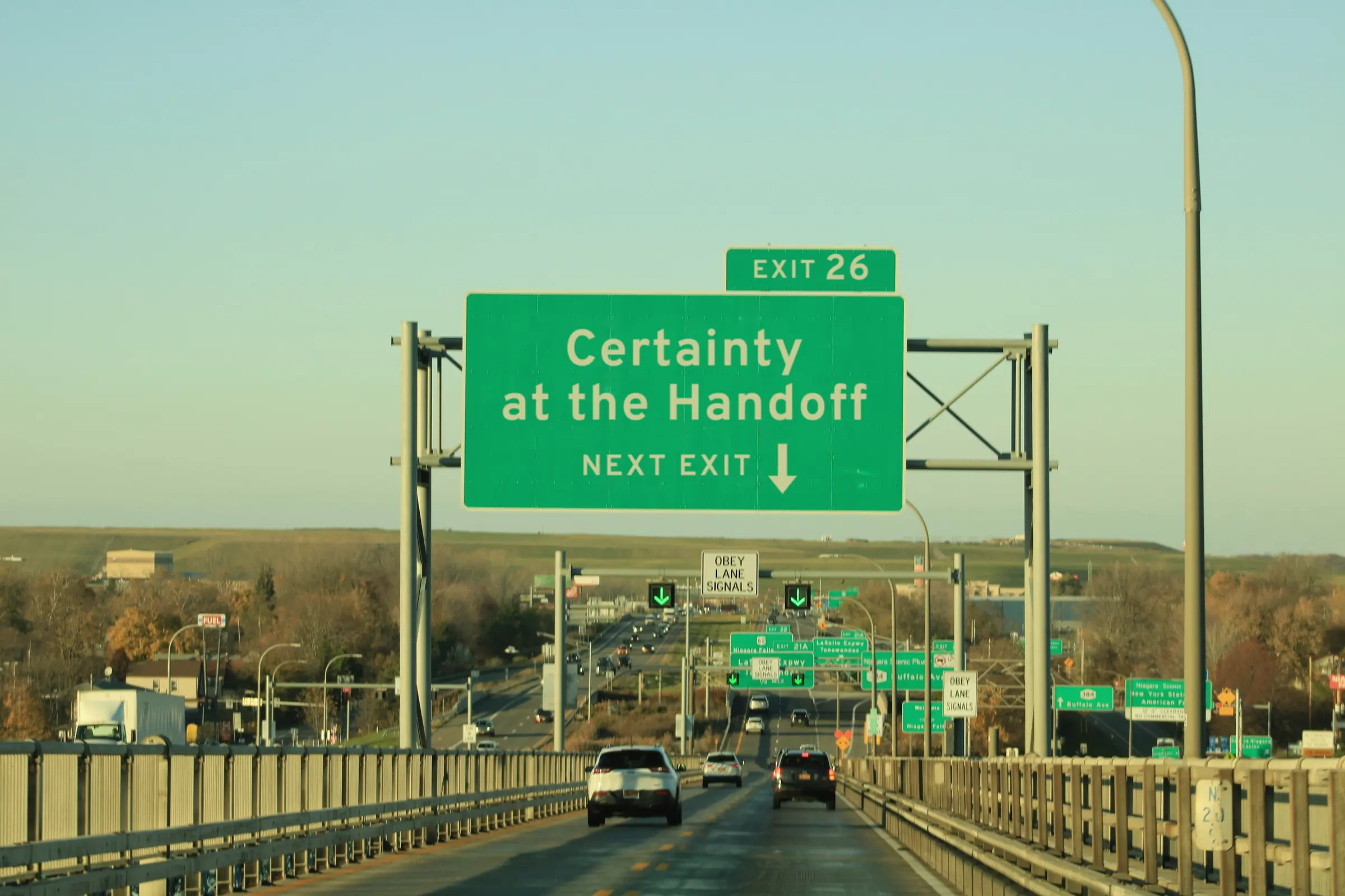An overhead highway sign reading Certainty at the Handoff, next exit, with the arrow pointing down to the lane below